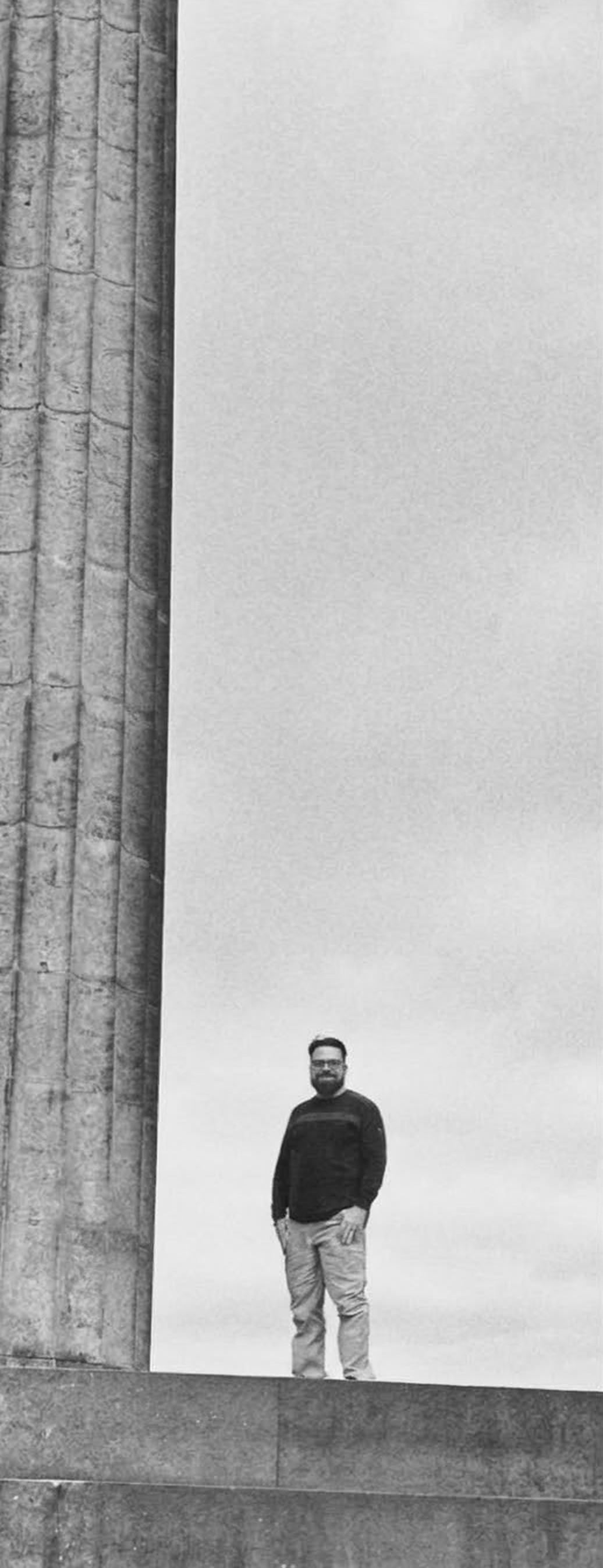 Jared standing beside a tall stone column under an overcast sky.