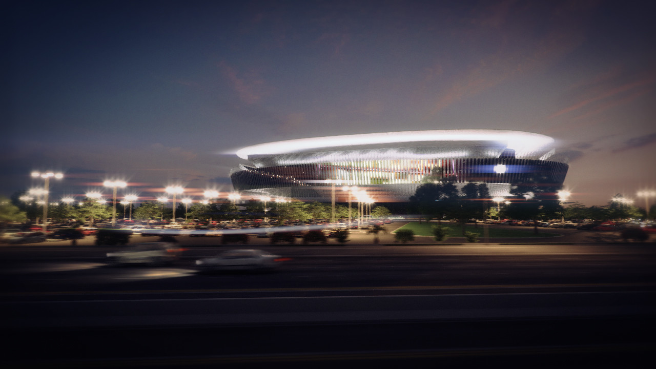 A lit stadium at dusk seen across a parking lot.